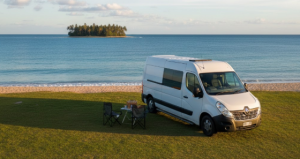 A white caravan parked on short green grass beside the calm tropical sea at St Helens Beach, Mackay, Queensland — an older couple in camp chairs watching the tide roll in at sunset, palm trees swaying gently, the warm colours of a tropical evening sky above — the relaxed rhythm of grey nomad life in Central Queensland.