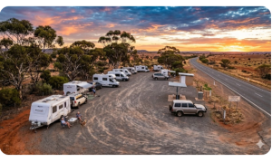 Roadside overnight parking rest area in rural Australia with caravans and campervans parked on gravel surrounded by eucalyptus trees at sunset