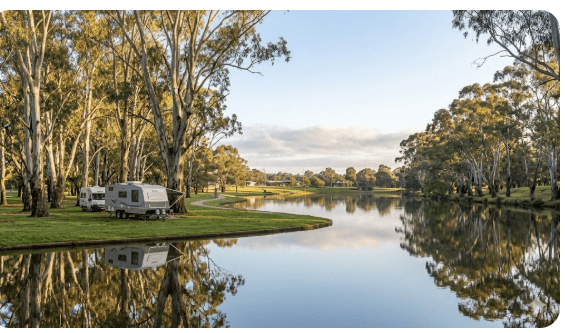 Shepparton rest areas on the Goulburn Valley Highway at Shepparton VIC 3630 — senior grey nomad guide 2026 showing Victoria Park Lake with flat grassed overnight camping area suitable for caravans motorhomes and campervans on the southbound Victorian grey nomad route Image Generation Prompt: Wide landscape photograph of Victoria Park Lake at Shepparton Victoria Australia in soft morning light. Flat grassed area beside a calm lake with gum trees reflecting in still water. One or two caravans parked quietly on the grass near the lake edge. Paved walking path visible in background. Authentic Australian regional travel photography — warm golden morning light, eucalyptus greens, pale blue sky, peaceful atmosphere.
